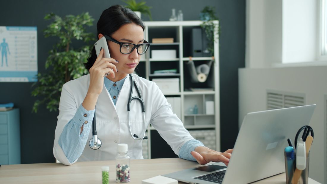 Physician on a call while working at a laptop